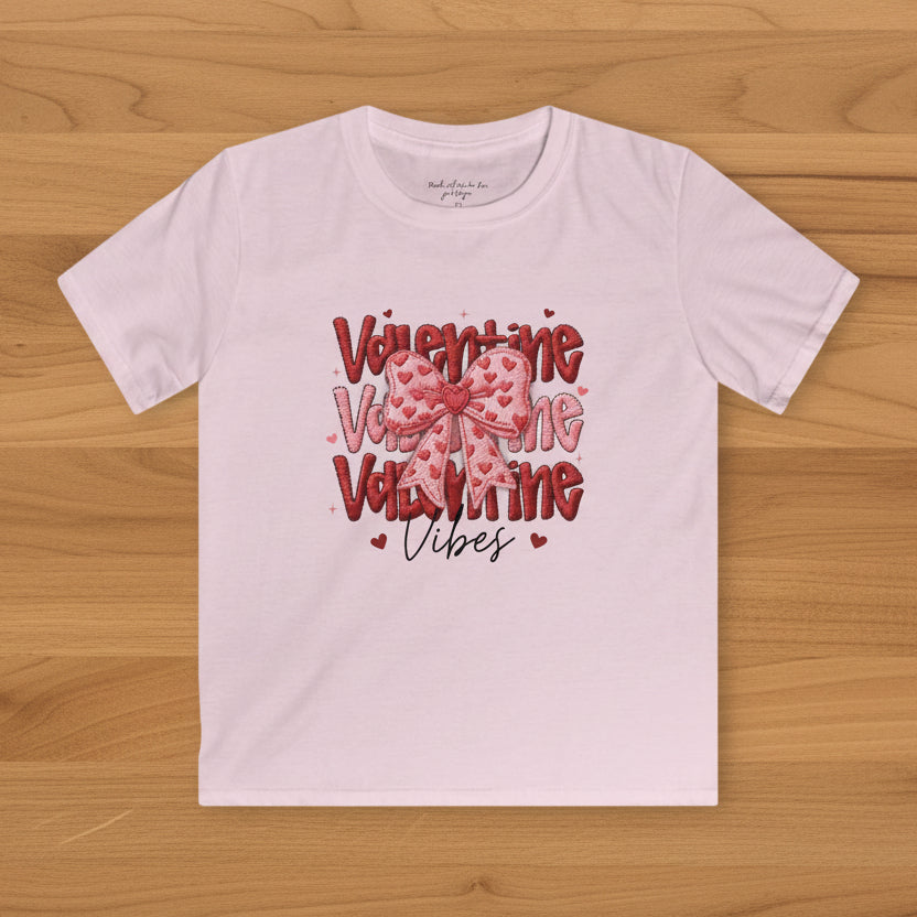 Pink t-shirt with Valentine's Day-themed text and graphics on a wood background