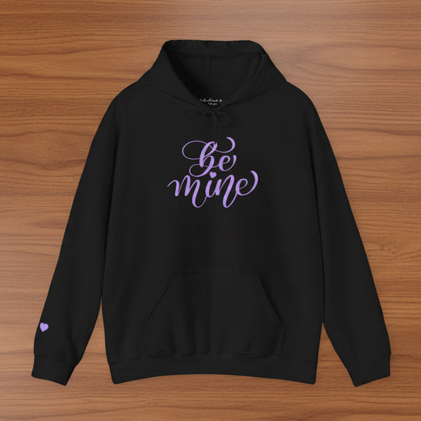 Black hoodie with 'be mine' text on a wooden surface